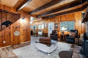 Interior de una cabaña de madera con escalera, chimenea, escritorio y una silla.