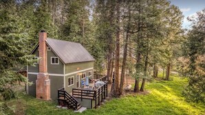 Eine Holzhütte mit Kamin aus Ziegeln, einer Terrasse und einer kleinen Veranda mit Sitzgelegenheit.