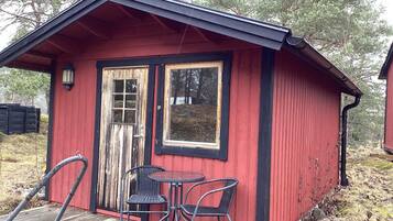 Una pequeña estructura de madera roja con una puerta, una ventana y una mesa con dos sillas.