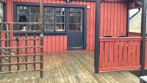 Un edificio de madera rojo con puerta y ventanas negras, una terraza de madera y un portón de metal.