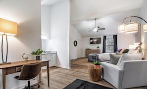 A modern apartment with a dining area, a sofa, a TV, a ceiling fan, and a large window.