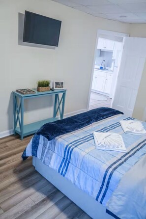 A bedroom with a bed, a small table with a plant, a TV on the wall, and a door leading to a bathroom.