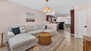 Una sala moderna con un sofá modular, una mesa de centro de madera y una cocina al fondo.