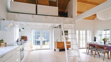 Um amplo loft com pé direito alto, cozinha, área de refeições com mesa e cadeiras e escada à vista.