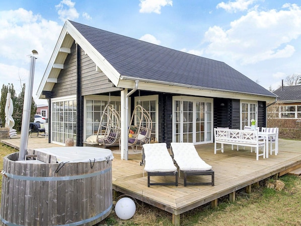 A house with a deck, outdoor seating, a hot tub, and a covered patio area.