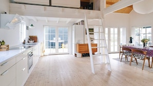A spacious loft with high ceilings, a kitchen with modern appliances, a dining area with a table and chairs, and a loft bed with storage. - 4 Star Holiday Home in Korsor (Korsor)