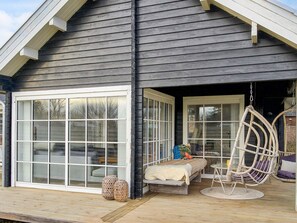 Een huis met een grote schuifpui, een veranda met een hangstoel en een kleine tafel.
