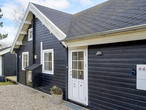 A black building with a white door and windows, a small outdoor seating area, and a gravel driveway. - 4 Star Holiday Home in Korsor (Korsor)