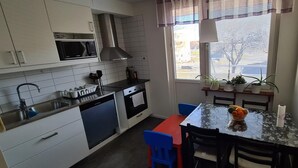 A compact kitchen with a microwave, stove, and sink. There's a dining table with chairs and a window with blinds. - 2 Bedroomapartment in Danderyd, City Stay (Danderyd)