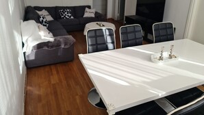 A modern living room with a white dining table, black chairs, a grey sofa with patterned cushions, a flat-screen TV, and a wooden floor. - 2 Bedroomapartment in Danderyd, City Stay (Danderyd)