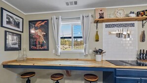 A kitchen with a wooden countertop, three stools, a window with curtains, a wine bottle, and a clock on the wall. - Vintage Vine Retreat w/ Private Studio ~walk Dtwn! (Murphys)