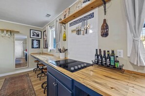 Una cocina con encimera de madera, cuchillos colgados y botellas de vino.