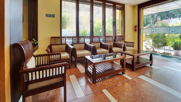 A lobby with wooden furniture, a fire exit sign, and large windows. - Super Townhouse Ernakulam North (Kanayannur)