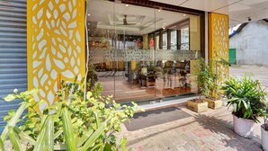 A modern building with a glass entrance, potted plants, and a visible interior with seating. - Super Townhouse Ernakulam North (Kanayannur)