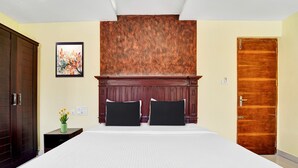 A hotel room with a large bed, a wooden headboard, a nightstand with a vase, and a door. - Super Townhouse Ernakulam North (Kanayannur)