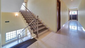 A hotel interior with a staircase, a fire exit sign, and a hallway leading to another room. - Super Townhouse Ernakulam North (Kanayannur)