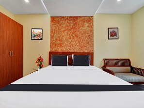 A hotel room with a large bed, a wooden wardrobe, a sofa, and two framed pictures on the walls.