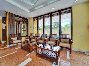 A lobby with wooden furniture, large windows, and a tiled floor.
