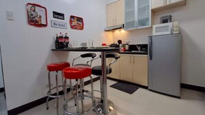 Eine kleine Küche mit Kühlschrank, Mikrowelle und Barhocker.