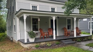 Ein zweistöckiges Haus mit Veranda, Hausnummer 34, mit Gartenbereich, Topfpflanzen und Gartenmöbeln.