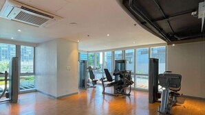 Une salle de sport spacieuse dotée d’un plancher en bois, d’équipements d’exercice et de grandes fenêtres laissant entrer la lumière naturelle.