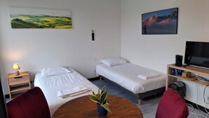 A hotel room with two single beds, a TV, a coffee maker, and a plant. - Quadruple hotel room (Lully)