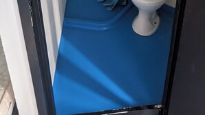 A small, enclosed bathroom with a shower, toilet, and blue floor mat. - Quadruple hotel room (Lully)