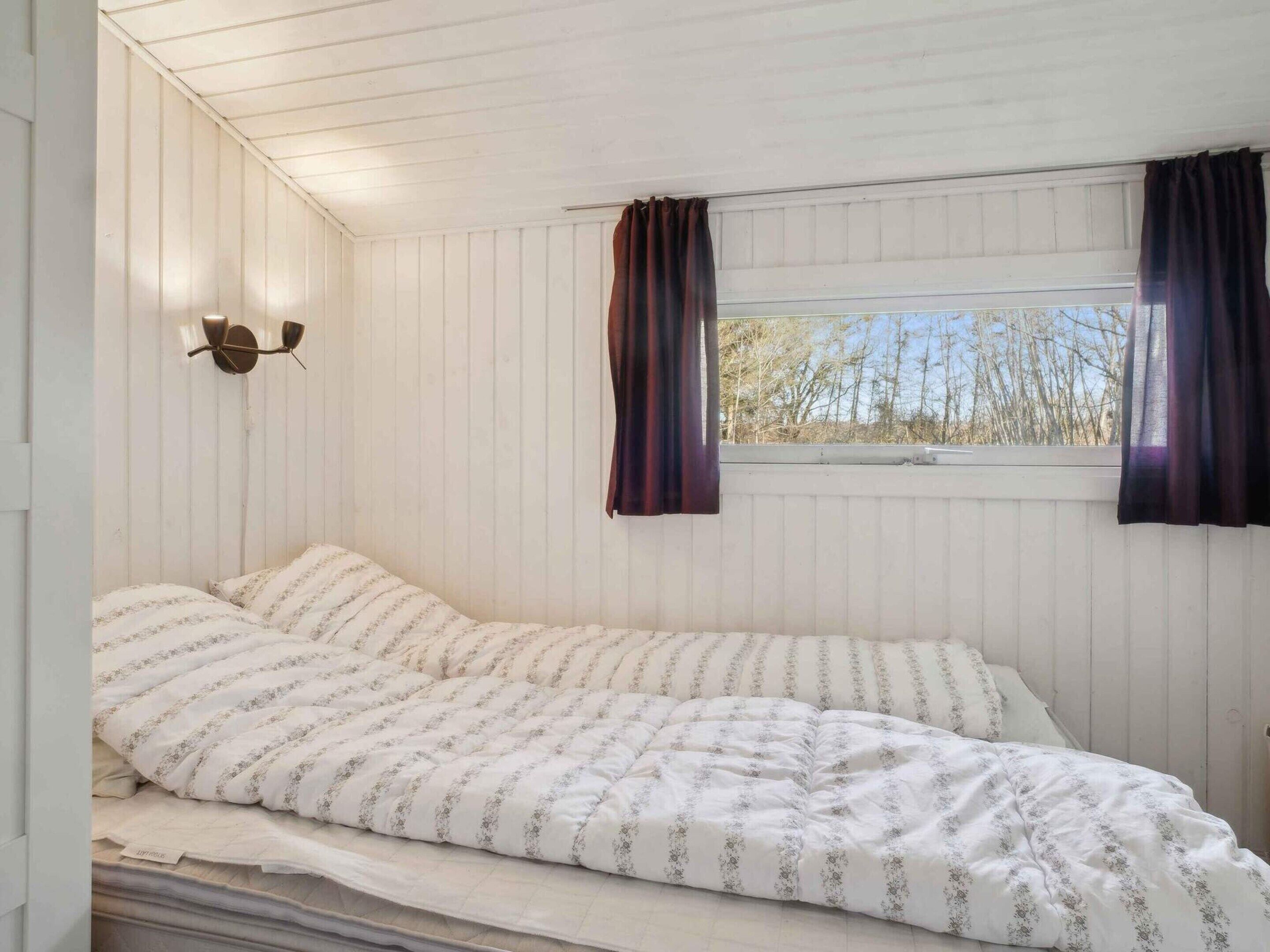 A single bed with a striped bedspread in a room with white paneled walls and a sloped ceiling.