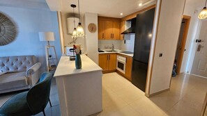 A modern kitchen with wooden cabinets, a black refrigerator, and a dining area with a sofa and chairs. - Unique by iulia (Oropesa del Mar)