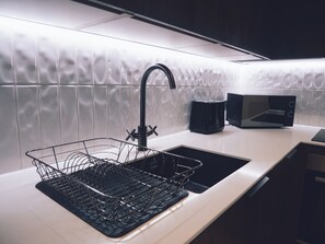 A kitchen with a black faucet, a black microwave, and a black dish rack on a white countertop. - Luxury 2 Bedroom Apartment in Jewellery Quarter - Garden Rooftop (Birmingham)