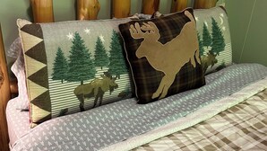 A bed with a plaid bedspread, two decorative pillows with forest and moose designs, and a wooden headboard. - Cozy cabin in the woods with internet, hot tub,fire pit, grille, gas stove (Walton)