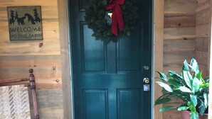 A cabin entrance with a dark wooden door, a welcome mat, a chair, and a potted plant. - Cozy cabin in the woods with internet, hot tub,fire pit, grille, gas stove (Walton)