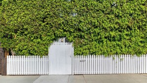 Een witte picket-hek met een poort, een metselpad en een haag op de achtergrond.
