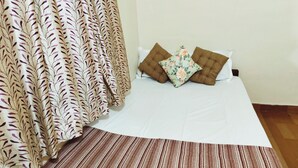 A bedroom with a bed, two pillows, a patterned curtain, and a striped rug.
