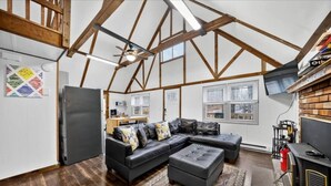 Ett rum i loftstil med synliga träbjälkar, en modulsoffa, en öppen spis och en tv.