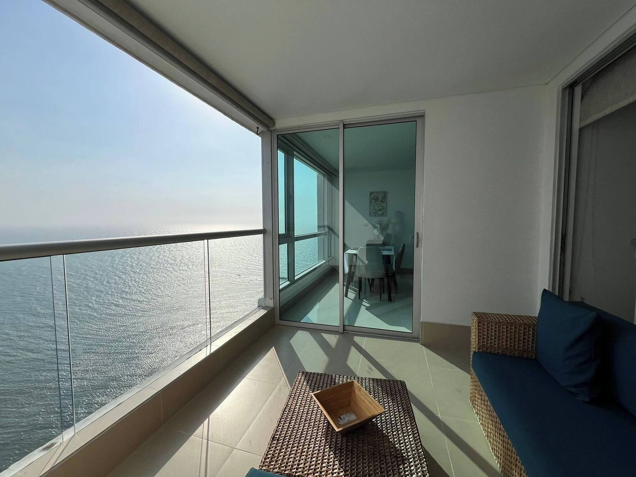 A balcony with a view of the sea, a dining area, and a sofa.