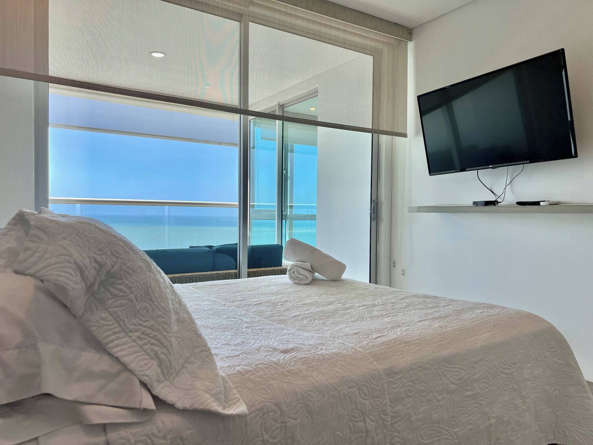 A hotel room with a bed, a television, and a view of the ocean.