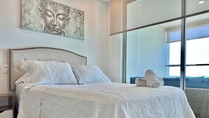A modern bedroom with a large bed, a headboard with decorative studs, a wall-mounted artwork, and a view through a glass door. - Palmetto Sunset Ocean Front Cartagena Laguito 2903 (Cartagena)