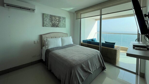 A modern bedroom with a bed, a desk, and a large window overlooking the sea. - Palmetto Sunset Ocean Front Cartagena Laguito 2903 (Cartagena)