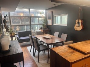 A modern dining area with a wooden table, chairs, and a guitar wall-mounted. - World Cup HQ: Dan Rockhill-Designed Luxury Apt, Lawrence's Coolest Neighborhood (Lawrence)