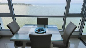 A dining area with a glass table and chairs, a plate with a decorative item, and a view of the sea through large windows. - Palmetto Sunset Ocean Front Cartagena Laguito 2904 (Cartagena)