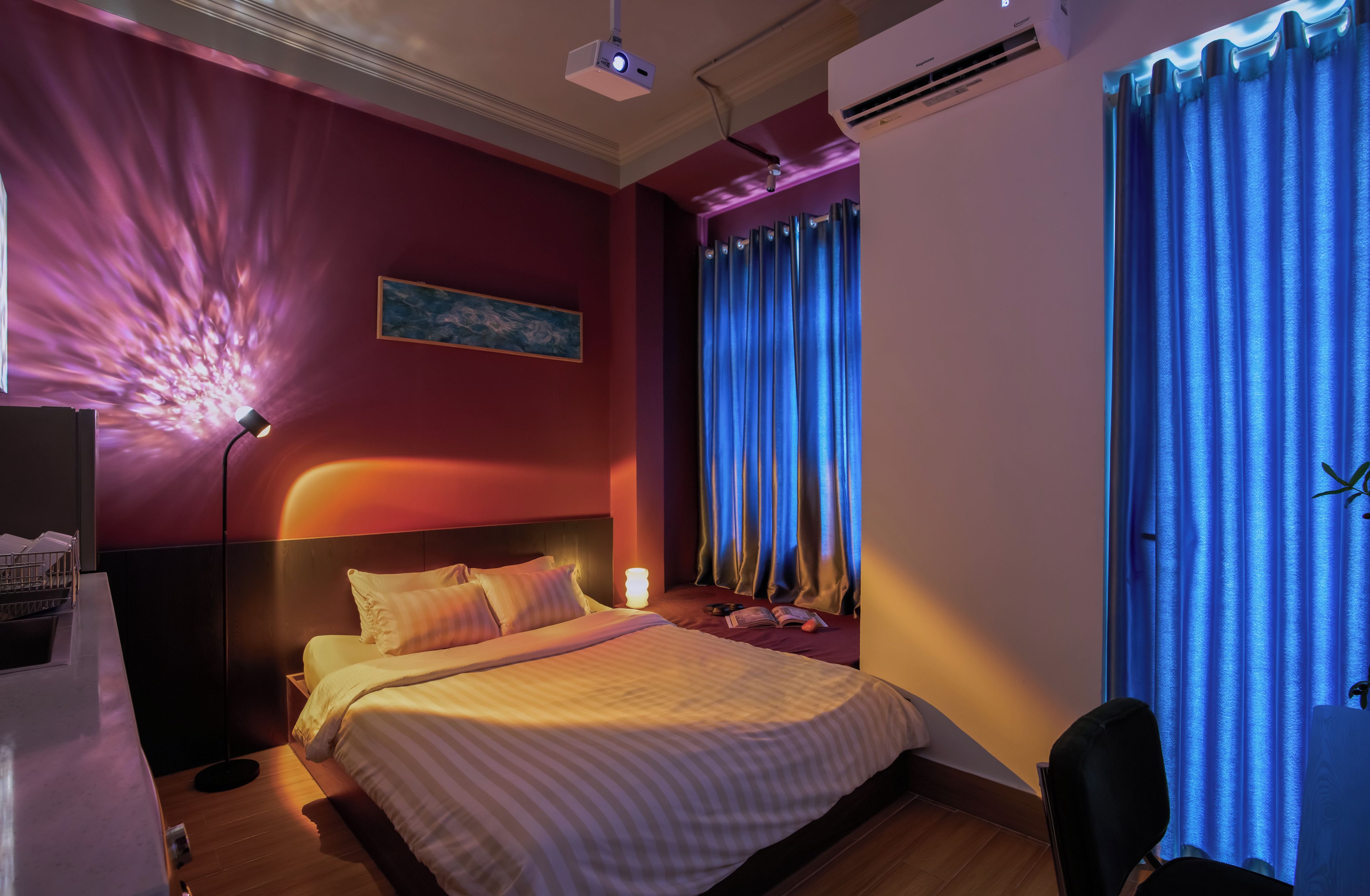 A hotel room with a bed, bedside table, lamp, air conditioning unit, and curtains.
