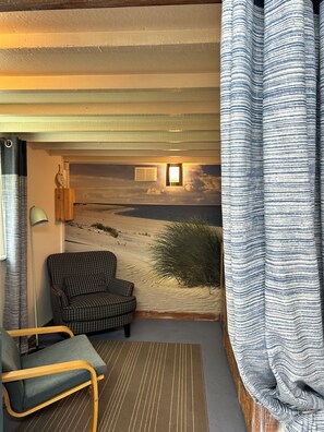 A room with a checkered sofa, a lamp, a view of a desert landscape, and a striped curtain.