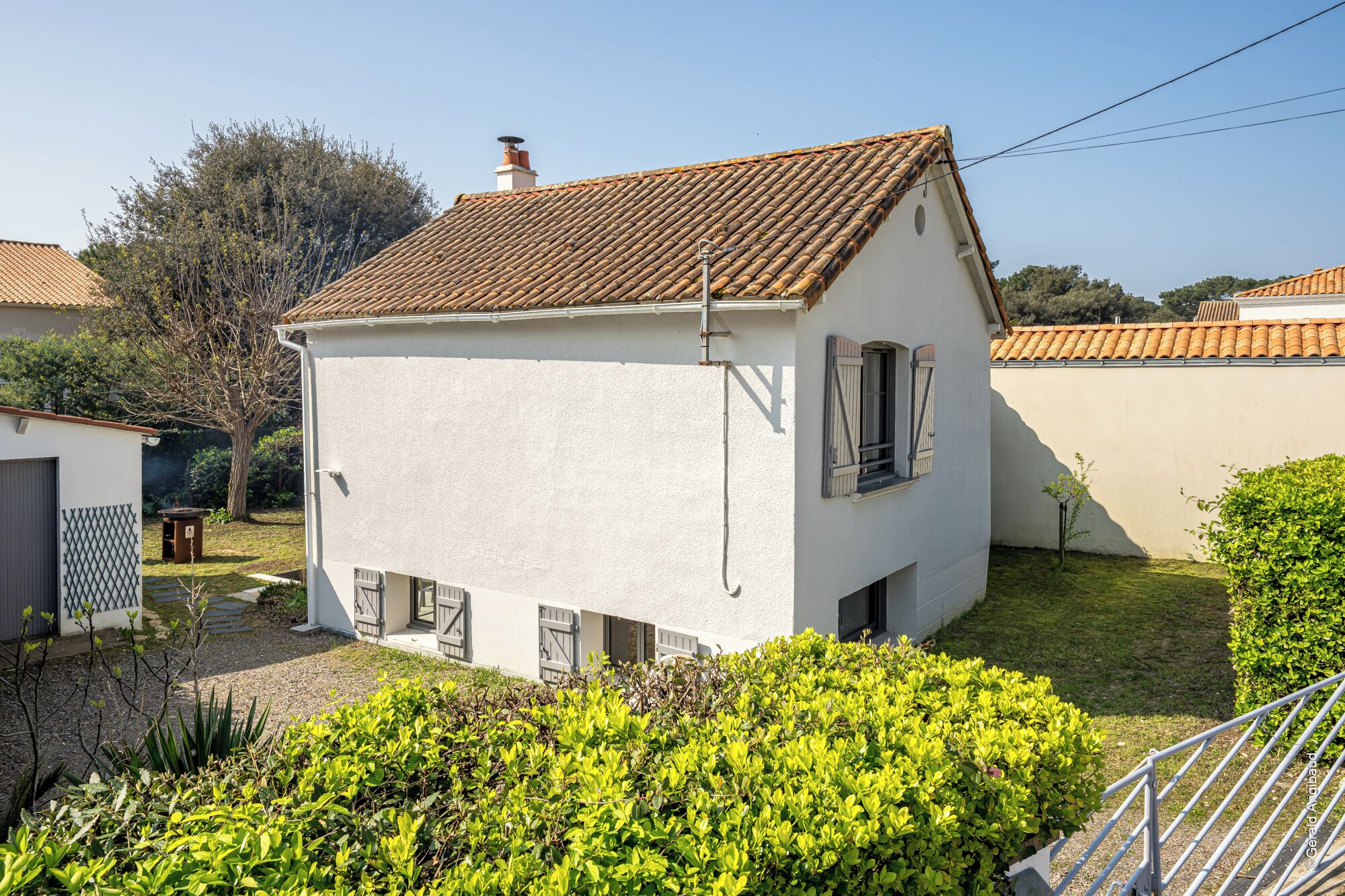 A single-story house with a tiled roof, a small garden, and a metal fence.