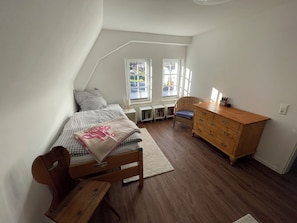 Une chambre avec un plafond en pente, un lit recouvert d’une couette à carreaux, une commode en bois et une chaise.