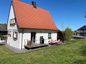 Un bâtiment blanc avec un toit rouge, un balcon et un petit espace extérieur aménagé avec des sièges.