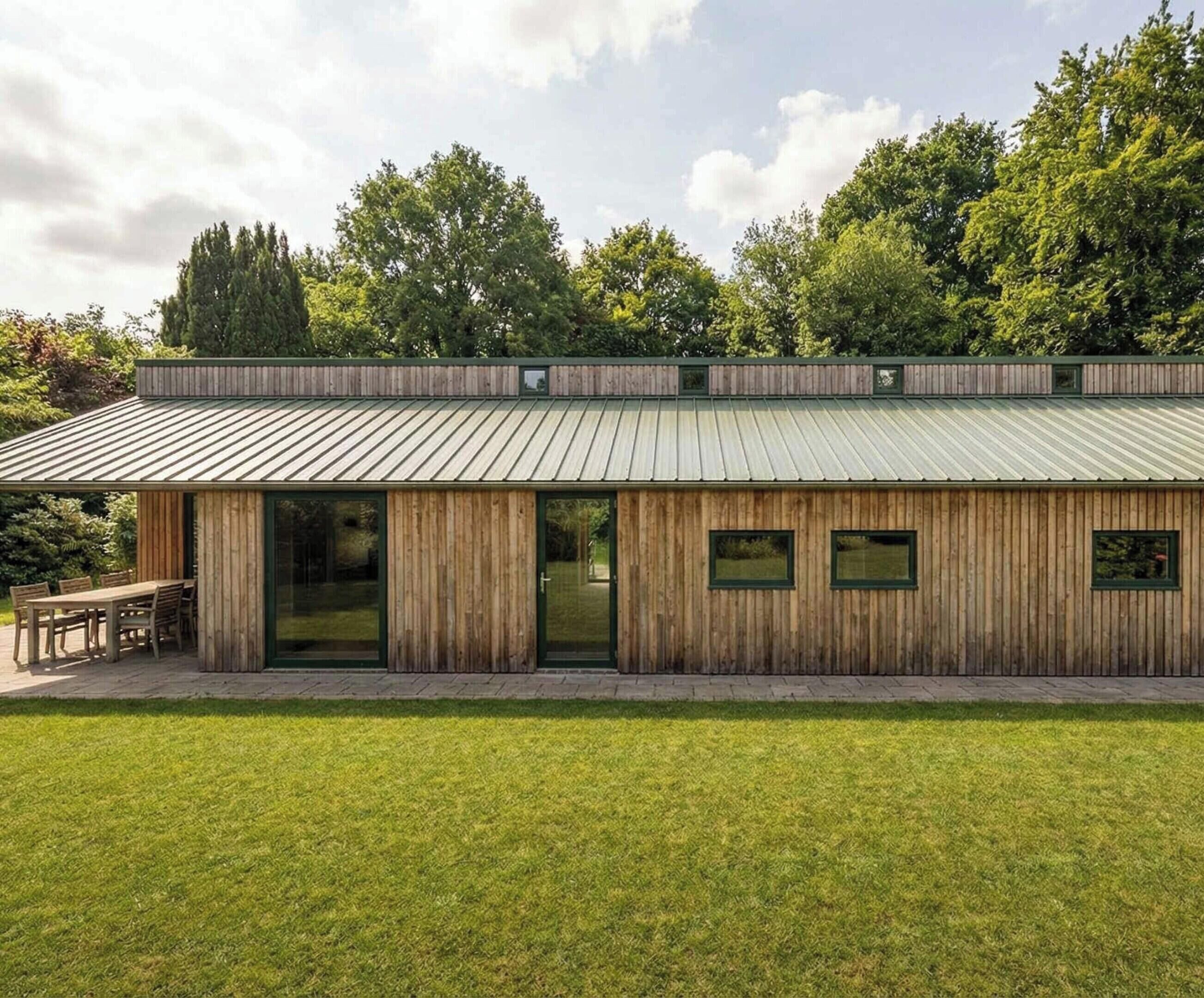 A modern wooden building with a metal roof, large windows, and a patio area.