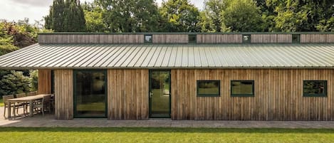 A modern wooden building with a metal roof, large windows, and a patio area.