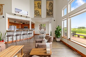A spacious living area with a kitchen, dining table, and large windows offering a view. - Bridger Mountain Vista-Private, Clean, Hot Tub, Stunning Rocky Mountain Views (Bozeman)