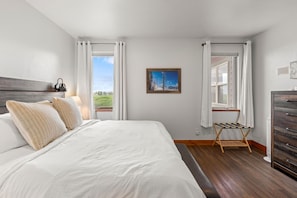 A bedroom with a bed, a window with curtains, a painting, and a dresser. - Bridger Mountain Vista-Private, Clean, Hot Tub, Stunning Rocky Mountain Views (Bozeman)